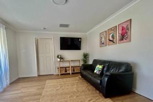 sala de estar con sofá de cuero negro y TV de pantalla plana en The Wildflower- Luxury Home Stay, en Utakarra