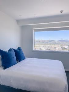 a white bed with blue pillows and a window at Sub-Penthouse on Gloucester - Highest rental in the South Island in Christchurch