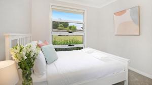 a white bedroom with a white bed and a window at Forest Brae in Bundanoon