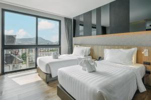 a hotel room with two beds and a large window at Rak Elegant Hotel Patong in Patong Beach
