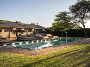 a swimming pool with chairs and umbrellas next to a house at Kuruman Lodge in Kuruman