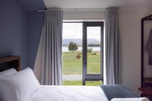a bedroom with a bed and a window with a view of a field at Haka House Lake Tekapo in Lake Tekapo