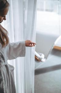 Eine Frau in einem weißen Gewand, die durch einen Vorhang schaut in der Unterkunft DIEDRICH Wellnesshotel & SPA - Adults only in Hallenberg