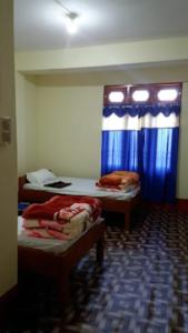 a room with two beds and a window with blue curtains at HOTEL DENGCHEM Bomdila in Bomdila