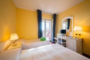 a bedroom with two beds and a desk with a television at Mendolia Beach Hotel in Taormina
