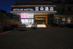 dos coches estacionados en un estacionamiento frente a un hotel en Atour Hotel Railway Station Dalian, en Dalian