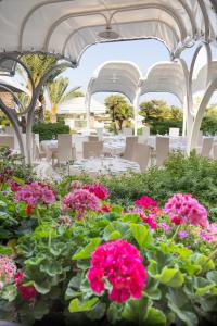 un patio con tavoli, sedie e fiori rosa di Hotel Baia Di Nora a Pula