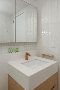W białej łazience znajduje się umywalka i lustro. w obiekcie Posh Perch on Collins - A Cosy Couple's Haven w Melbourne