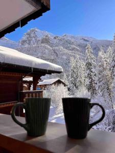 two coffee cups sitting on a table with snow covered trees at Peacefull Mountains View in Kandersteg