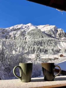 two coffee cups sitting on a window sill with a mountain at Peacefull Mountains View in Kandersteg