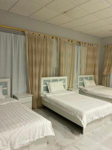 two beds in a bedroom with white sheets and curtains at شالية ألأمراء 