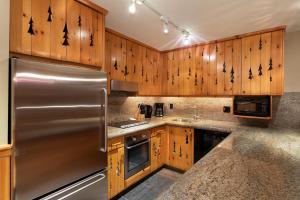 a kitchen with wooden cabinets and a stainless steel refrigerator at Hearthstone Lodge 3 - Central Village Condo with Private Sauna & Hot Tub - Whistler Platinum in Whistler