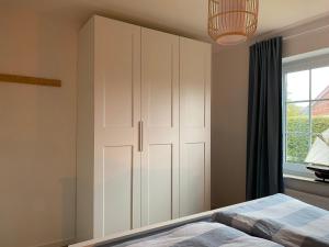 ネスマージールにあるNessmersiel, Renovierte Erdgeschosswohnung mit Garten, in Deichnähe, Wallbox,の白いキャビネットと窓付きのベッドルーム1室