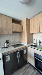 Una cocina con gabinetes de madera y un refrigerador negro. en Depto nuevo en republica cercano al movistar arena, en Santiago
