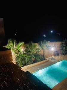una piscina notturna con palme di Villa Maison des Arts - Oasis de Calme et Tranquillité Près de l'Aéroport d'Essaouira a Essaouira