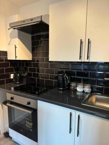una cocina con armarios blancos y una pared de azulejos negros en Apartment Close to the Studios en Borehamwood