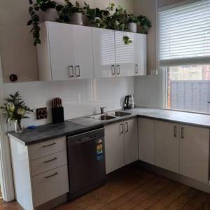 kuchnia z białymi szafkami, umywalką i oknem w obiekcie North Perth Stylish Abode CBD w mieście Perth