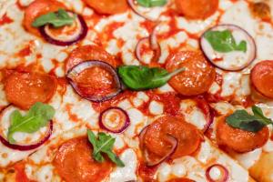 a close up of a pizza with pepperoni and onions at PANORAMA SportHOTEL in Folgaria