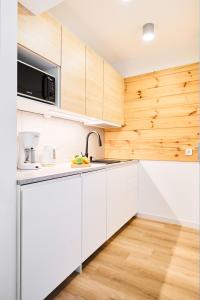 a kitchen with white cabinets and wooden walls at MikroApartamenty Zakopane Chramcówki by RentiloPL in Zakopane