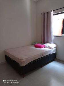 Bett mit rosa Kissen in einem Zimmer mit Fenster in der Unterkunft casa com piscina, 03 quartos, ótima localização! in Bonito