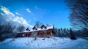Nadleśniczówka - Bieszczadzka Zagroda في Weremień: منزل خشبي مغطى بالثلج على تلة