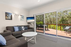 a living room with a couch and a table and a balcony at Rocks Place by Experience Jervis Bay in Vincentia