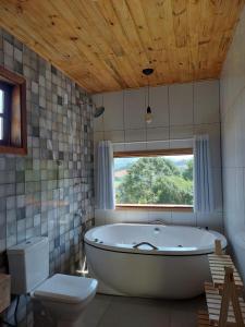 a bathroom with a tub and a toilet and a window at Chalés Cantinho do Céu in Monte Verde
