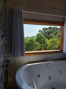 uma banheira na casa de banho com uma janela em Chalés Cantinho do Céu em Monte Verde