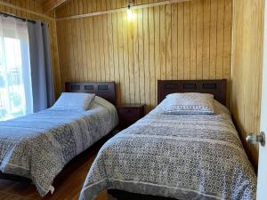 two beds in a room with wooden walls at Comodidad y hermosa vista volcán in Melipeuco