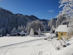 a snow covered village with a yellow house and trees at Alpenloft Theresia in Ferlach