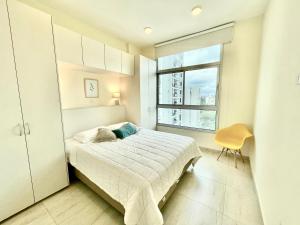 a white bedroom with a bed and a window at Villa morra, a pasos de los shoppings! in Asunción