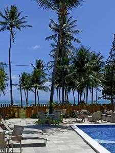 einen Pool mit Stühlen, Palmen und dem Meer in der Unterkunft Beira-mar Tamandaré / Carneiros in Tamandaré