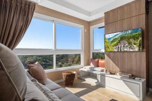 ein Wohnzimmer mit einem TV und großen Fenstern in der Unterkunft Jardins de Gramado 402 B - 3 suítes e linda vista in Gramado