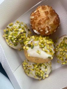 Merlin Malga San Giorgio 6 في بوسكو تيسانيوفا: ثلاث قطع دونات مغطاة بكريمة بيضاء ومزينة بحبيبات خضراء في علبة