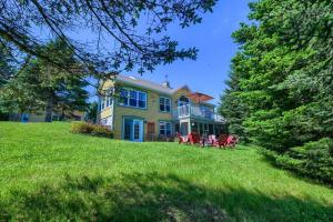 une grande maison jaune avec des chaises rouges sur une pelouse dans l'établissement Stunning Waterfront Chalet A Lot Of Natural Light, à Saint-Zénon