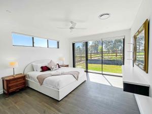 a white bedroom with a bed and a large window at Casa Divina in Pokolbin