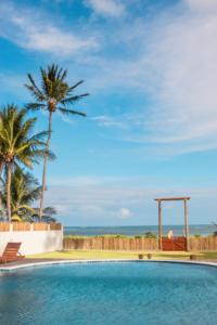 a swimming pool with a palm tree and the ocean at POUSADA E RESTAURANTE GAROUPA in São Miguel dos Milagres