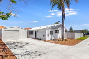 a white house with a garage and a palm tree at Fairbairn Family Beach Bungalow in Busselton