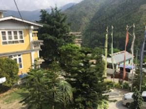 a yellow house with trees in front of a mountain at Hotel Keeduk Inn Dirang in Dirang Dzong