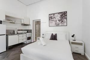 a white bedroom with a large bed and a kitchen at Stroll To Fremantle's Core Studio Apartment in Fremantle