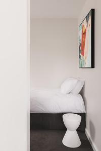 a bedroom with a white bed and a white stool at MAC St Kilda by Melbourne Apartment Collection in Melbourne