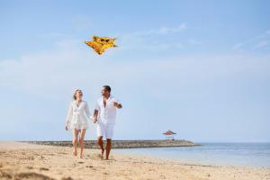 فندق وسبا نوسا دوا بيتش، بالي في نوسا دوا: رجل وامرأة يسيران على الشاطئ بالطائرة الورقية