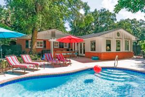 a pool with chairs and umbrellas in front of a house at 120 Druid Oaks Lane in Saint Simons Island