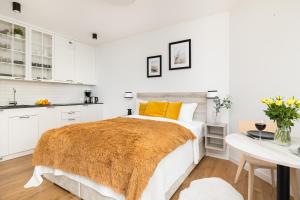 a white bedroom with a bed with an orange blanket at Sunny Coast Studio in Pobierowo by Renters in Pobierowo