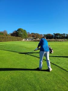 un hombre balanceando un club de golf en un campo verde en New Forest Bees Holiday Home, Bashley, en New Milton