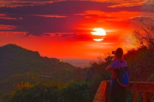una persona de pie en un banco viendo la puesta de sol en Family Batcave Homestay, en Battambang