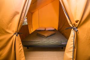 a small bed in a tent with curtains at CAMPING ONLYCAMP DES HALLES in Decize