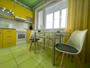 een keuken met gele kasten en een glazen tafel en stoelen bij Уютная Квартира с ванной. in Pavlodar