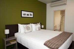 a bedroom with a large white bed with green walls at Quest Rotorua Central in Rotorua