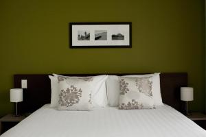 ein Bett mit weißen Kissen und einer grünen Wand in der Unterkunft Quest Rotorua Central in Rotorua